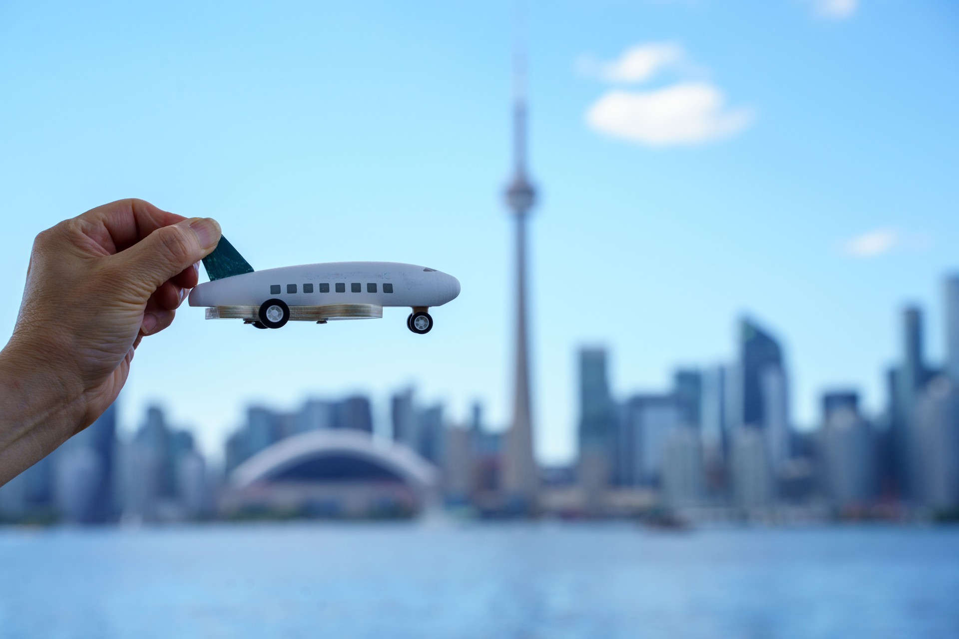 Toy airplane in hand against the background of the Toronto downtown skyline and the CN Tower in the background. Passenger traffic and flights to dream vacation