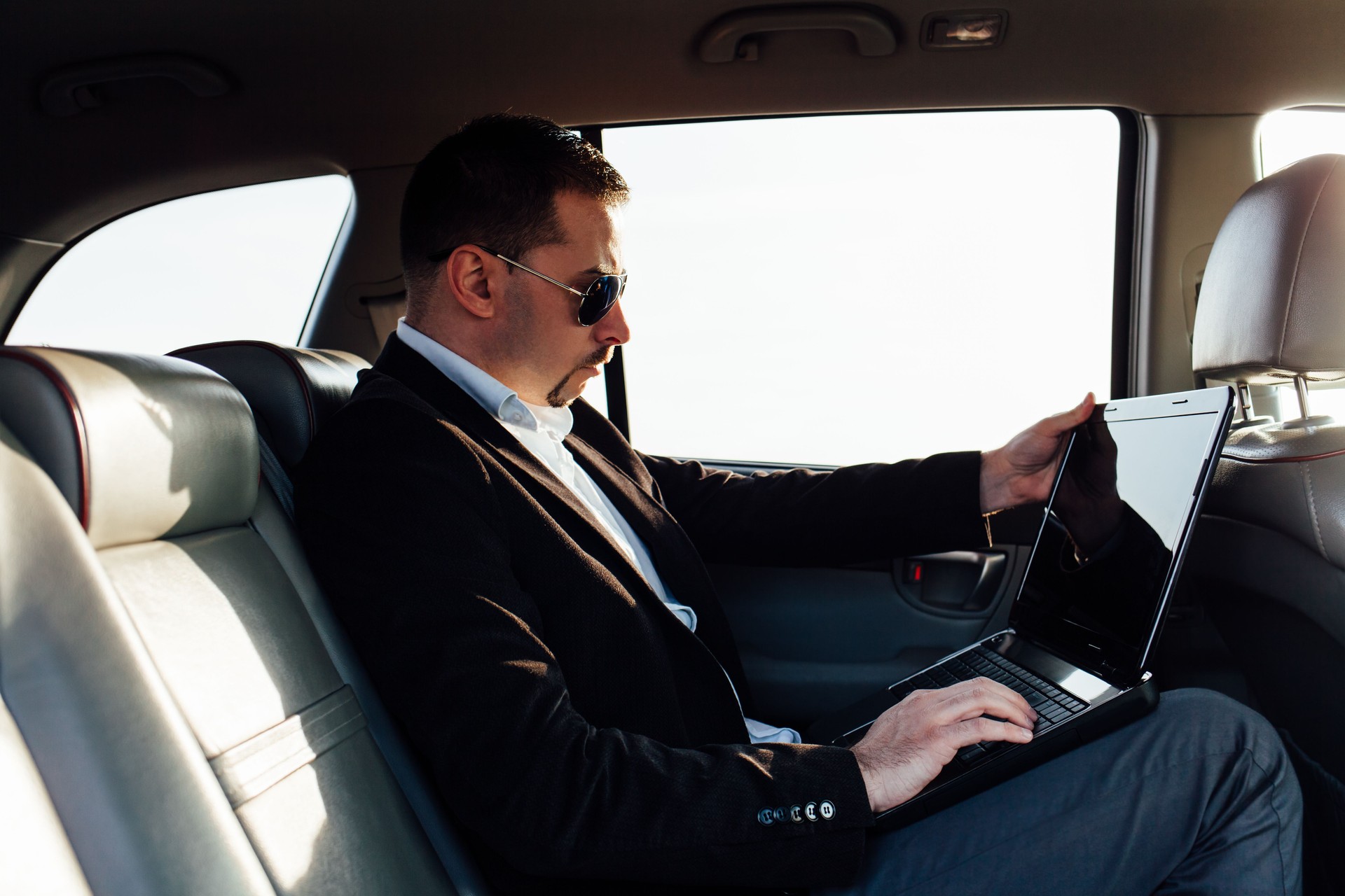 Businessman using laptop on the backseat of luxurious car